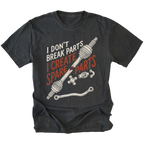 A black graphic t-shirt featuring a humorous design with the text 'I DON'T BREAK PARTS I CREATE SPARE PARTS' in white and orange, accompanied by illustrations of car steering column and brake line components.