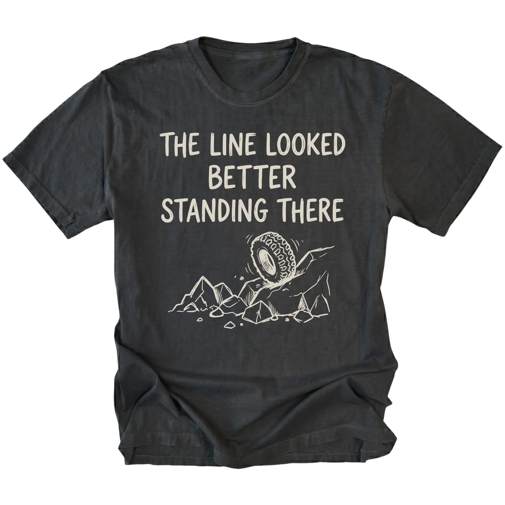 Black T-Shirt with hand-drawn tire and rocks graphic and text reading “The Line Looked Better Standing There” shown on front view by Trail Snark.