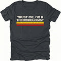Black t-shirt with retro stripes and the phrase “Trust Me, I’m a Tacomaologist” printed on the front by Trail Snark.