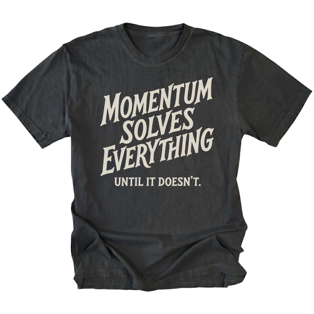 A black short-sleeve t-shirt with a distressed cream-colored graphic text that reads 'MOMENTUM SOLVES EVERYTHING UNTIL IT DOESN'T.' on a solid white background.