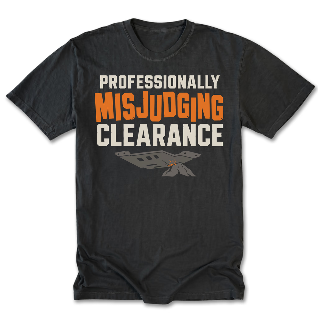 A black t-shirt with a graphic print reading 'PROFESSIONALLY MISJUDGING CLEARANCE' in white and orange lettering, featuring a small gray and orange airplane graphic below, displayed on a clean white background.