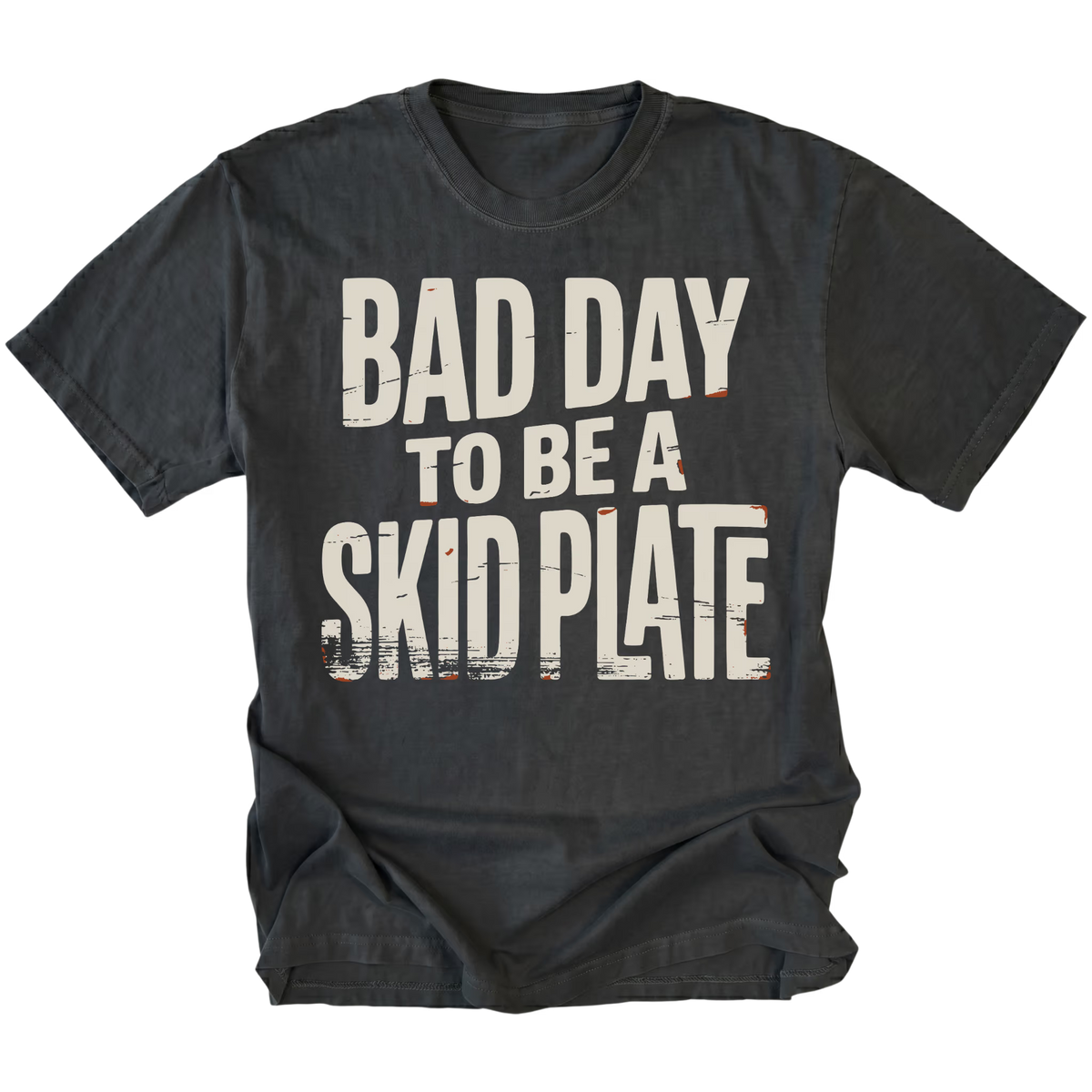 A black graphic t-shirt with the text 'BAD DAY TO BE A SKID PLATE' printed in distressed off-white lettering with small orange road-striping accents, shown on a plain white background.