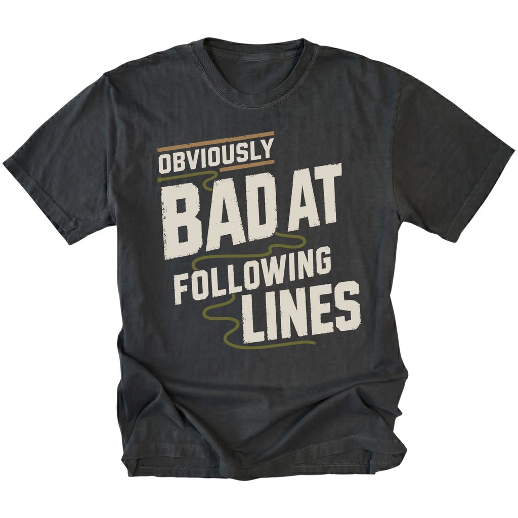A black graphic t-shirt with the text 'OBVIOUSLY BAD AT FOLLOWING LINES' printed on the front in distressed off-white lettering with olive green accents, shown against a plain white background.