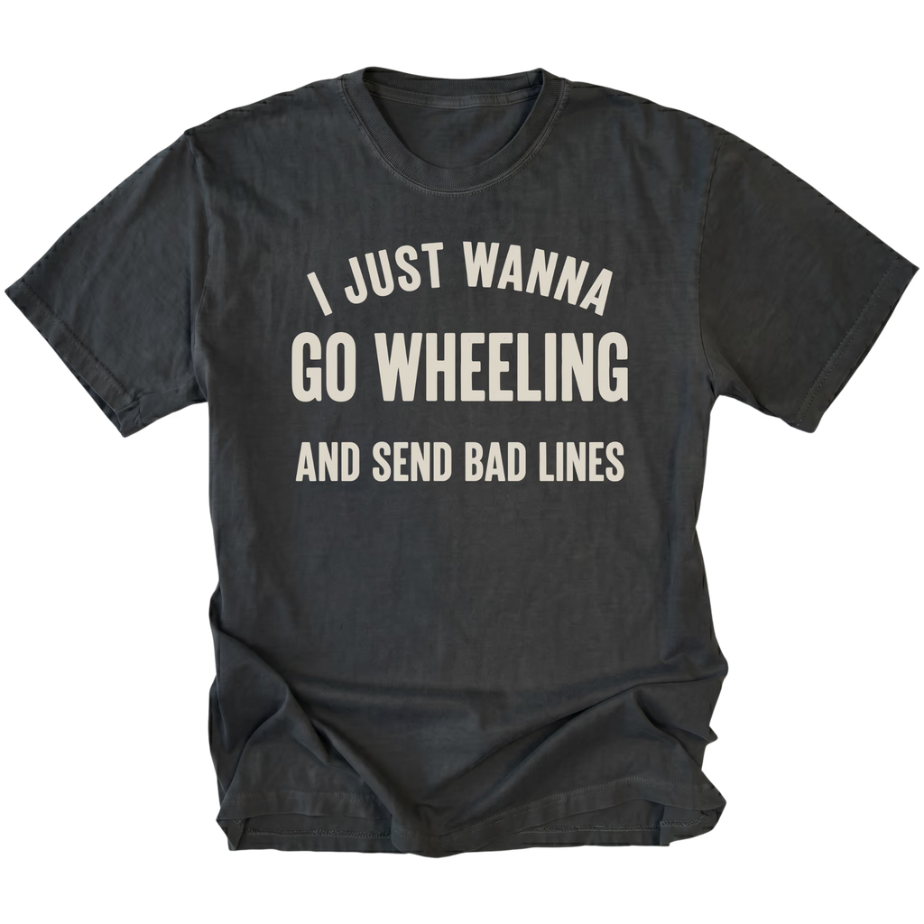 A black t-shirt with distressed cream-colored text that reads 'I JUST WANNA GO WHEELING AND SEND BAD LINES' printed on the front, displayed against a solid white background.