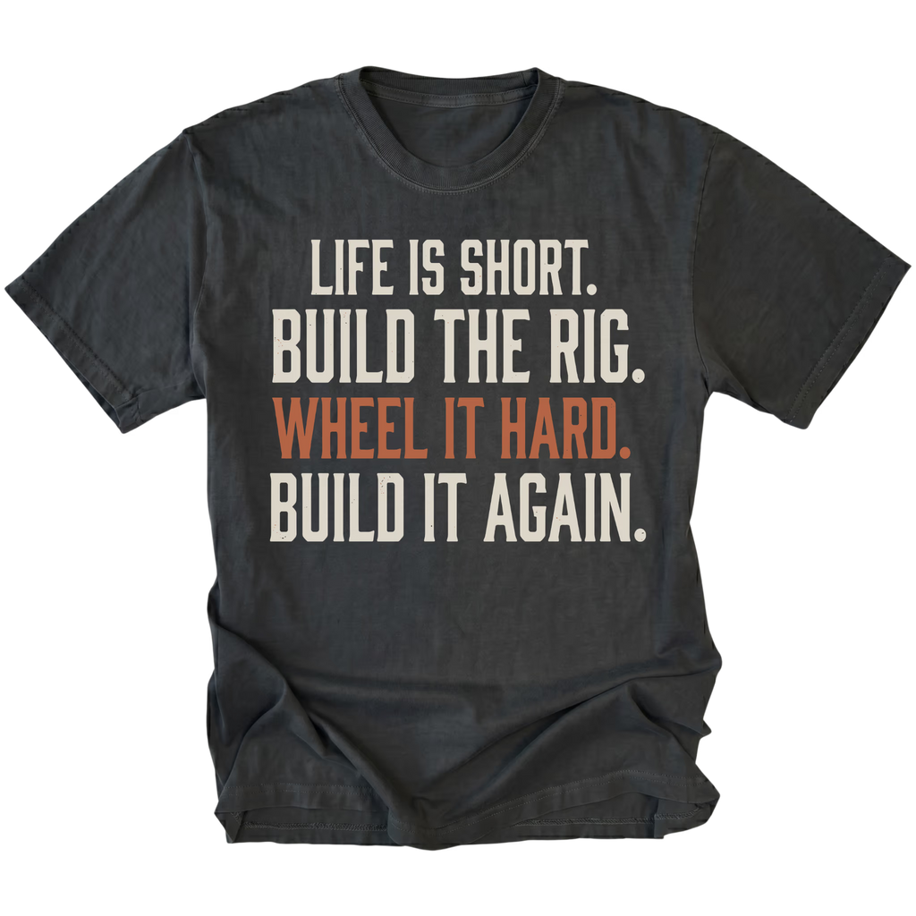 A black short-sleeve t-shirt with a distressed white and orange text graphic on the front reading 'LIFE IS SHORT. BUILD THE RIG. WHEEL IT HARD. BUILD IT AGAIN.'