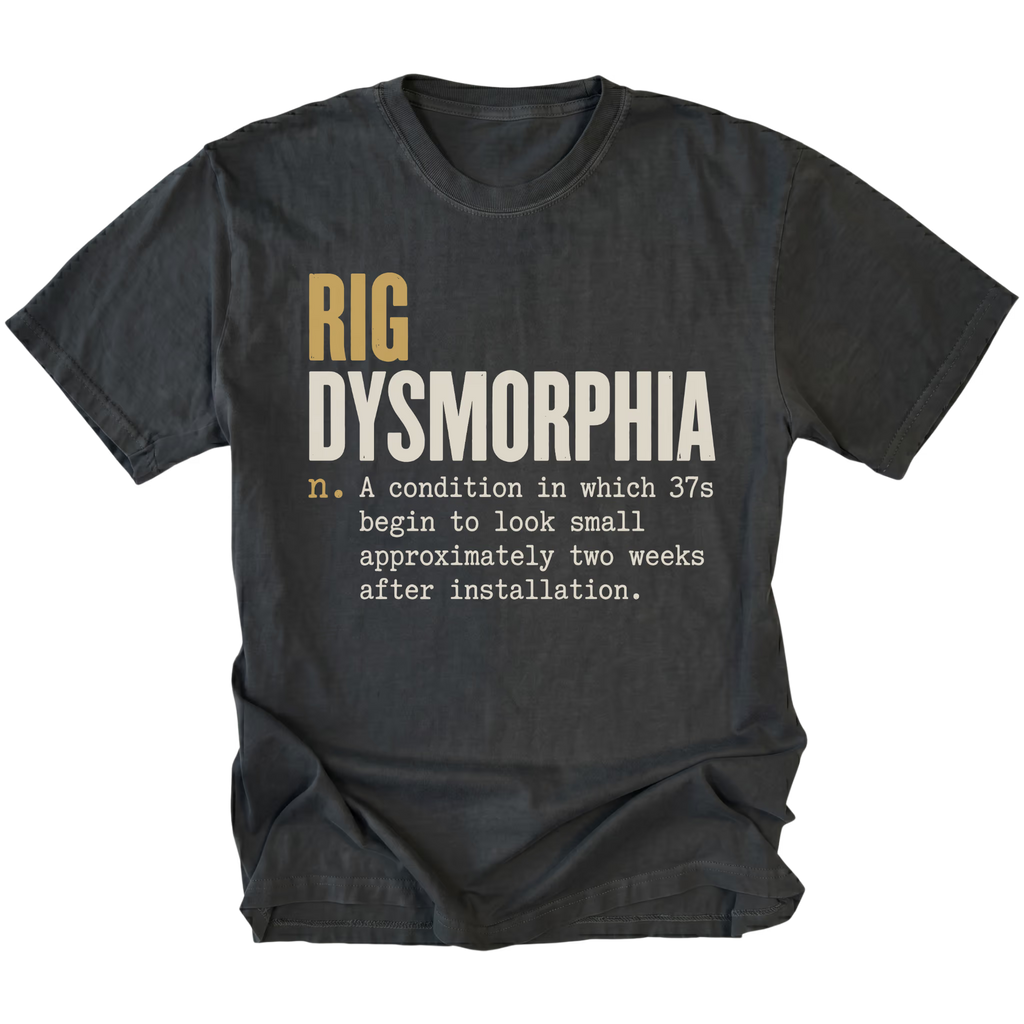A black graphic t-shirt laid flat on a white background. The shirt features a humorous definition printed on the front: 'RIG DYSMORPHIA' in gold and white block letters, followed by a smaller white typewriter-style definition.