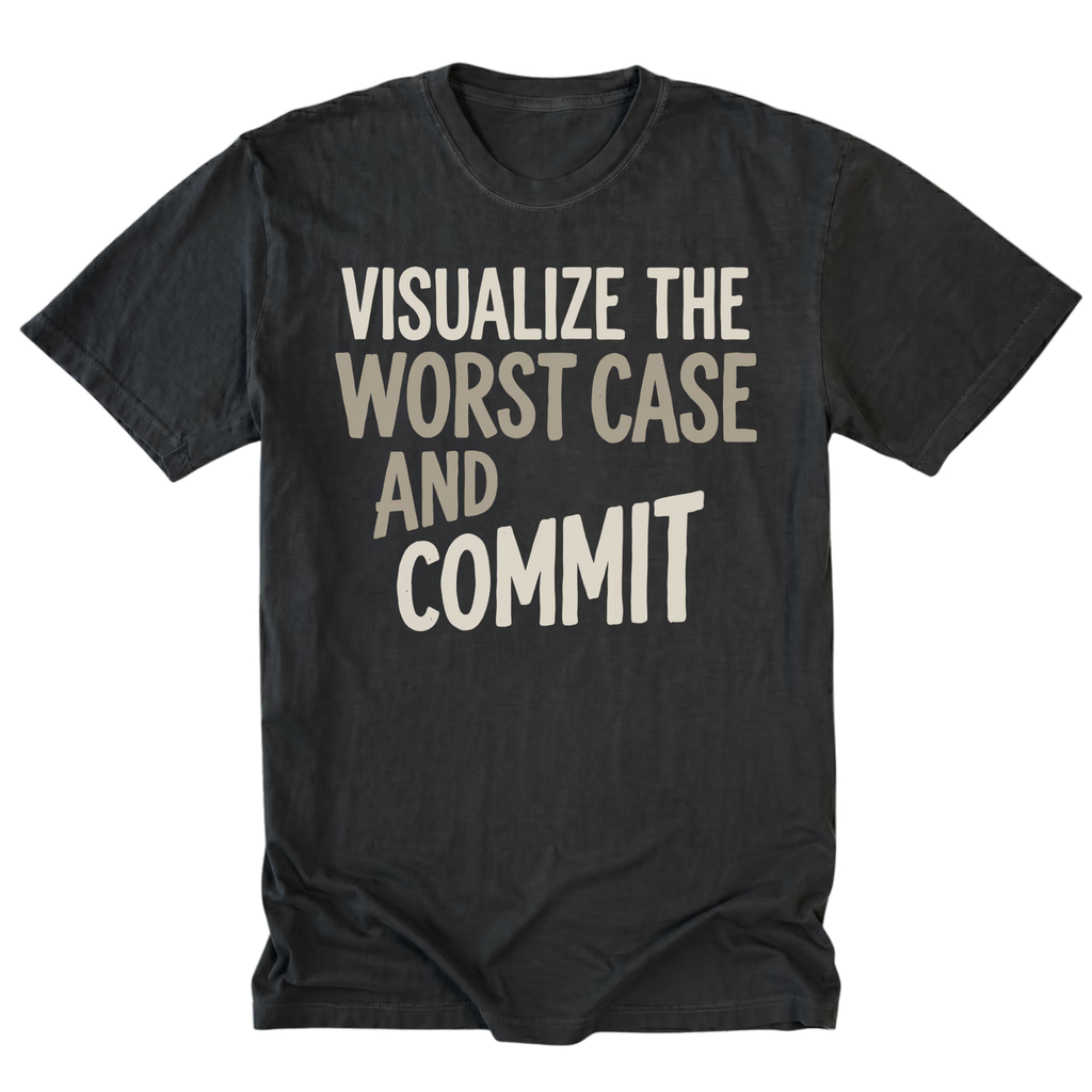 A black tall t-shirt with a distressed graphic print that reads 'VISUALIZE THE WORST CASE AND COMMIT' in cream-colored text, displayed flat against a solid white background.