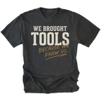 A black t-shirt with a distressed graphic print that reads 'WE BROUGHT TOOLS BECAUSE WE KNOW US.' in cream and tan lettering, displayed on a solid white background.
