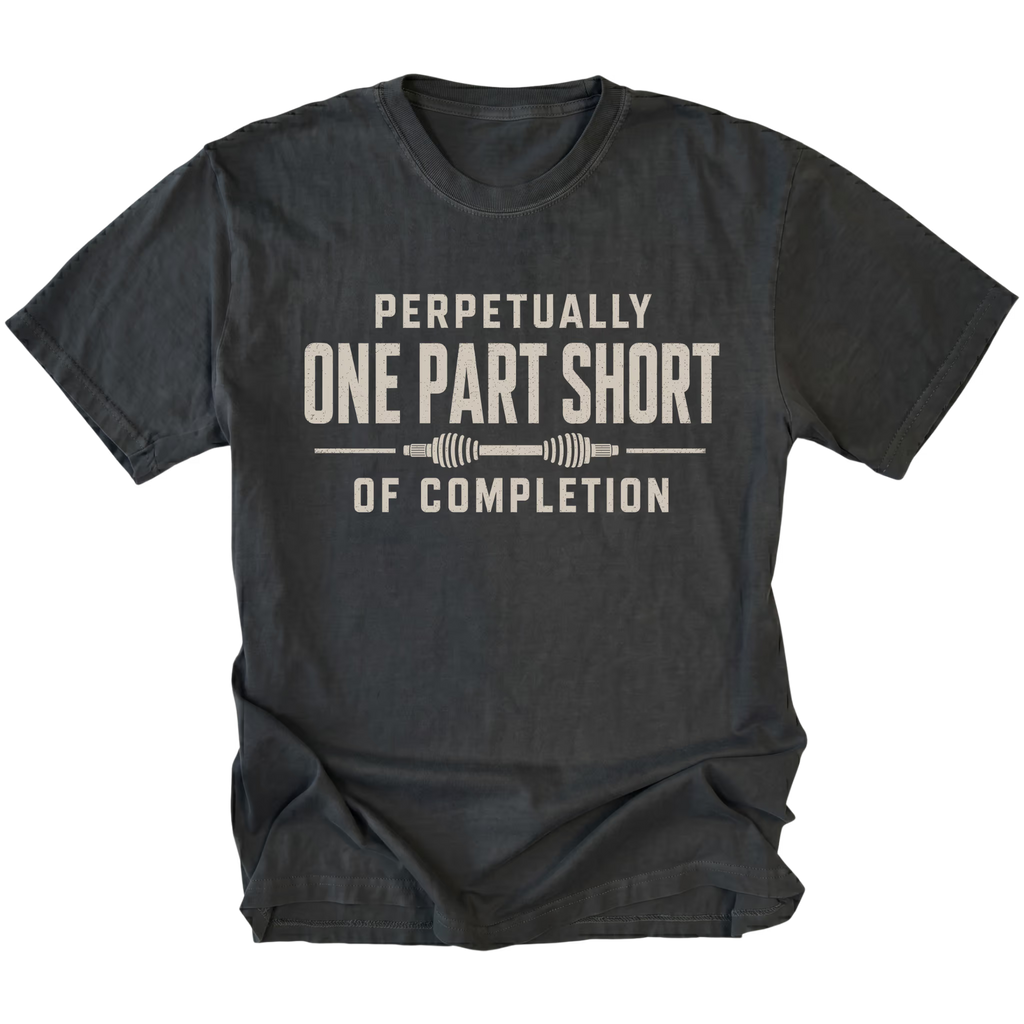 Black T-shirt with a Perpetually One Part Short Of Completion garage build design shown from the front by Trail Snark.