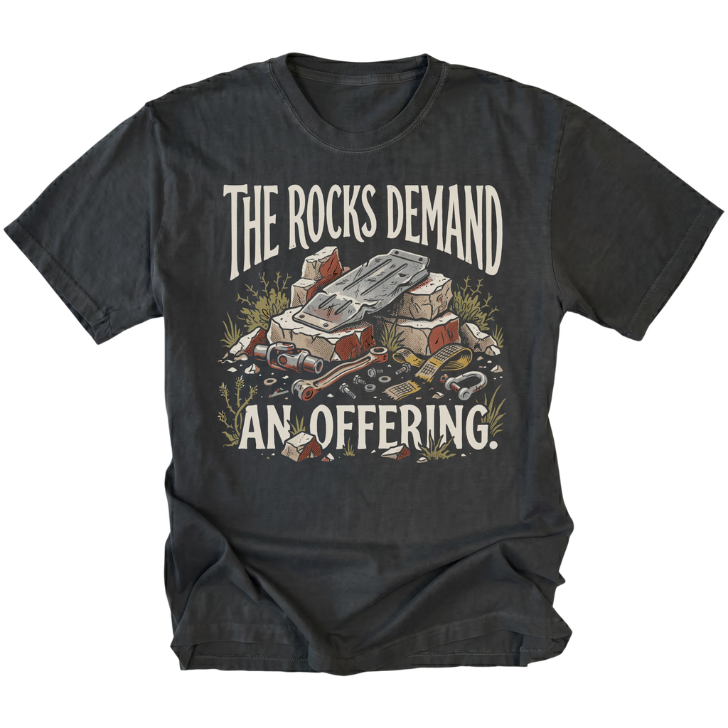 A black graphic t-shirt featuring a vintage-style illustration of a pile of rocks and gold coins with the text 'THE ROCKS DEMAND AN OFFERING.' printed in distressed cream lettering.