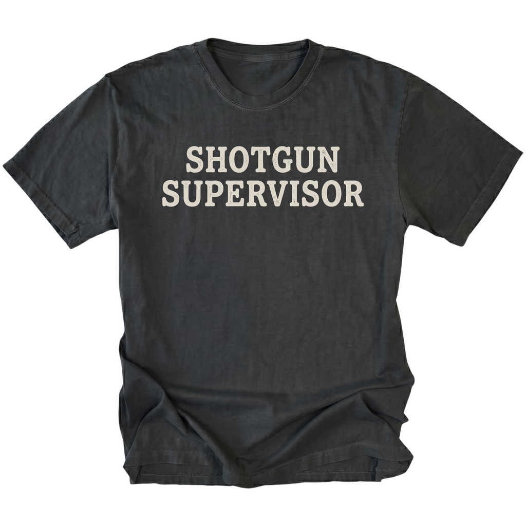 A black t-shirt with the words 'SHOTGUN SUPERVISOR' printed in a distressed off-white font across the chest, displayed flat against a solid white background.