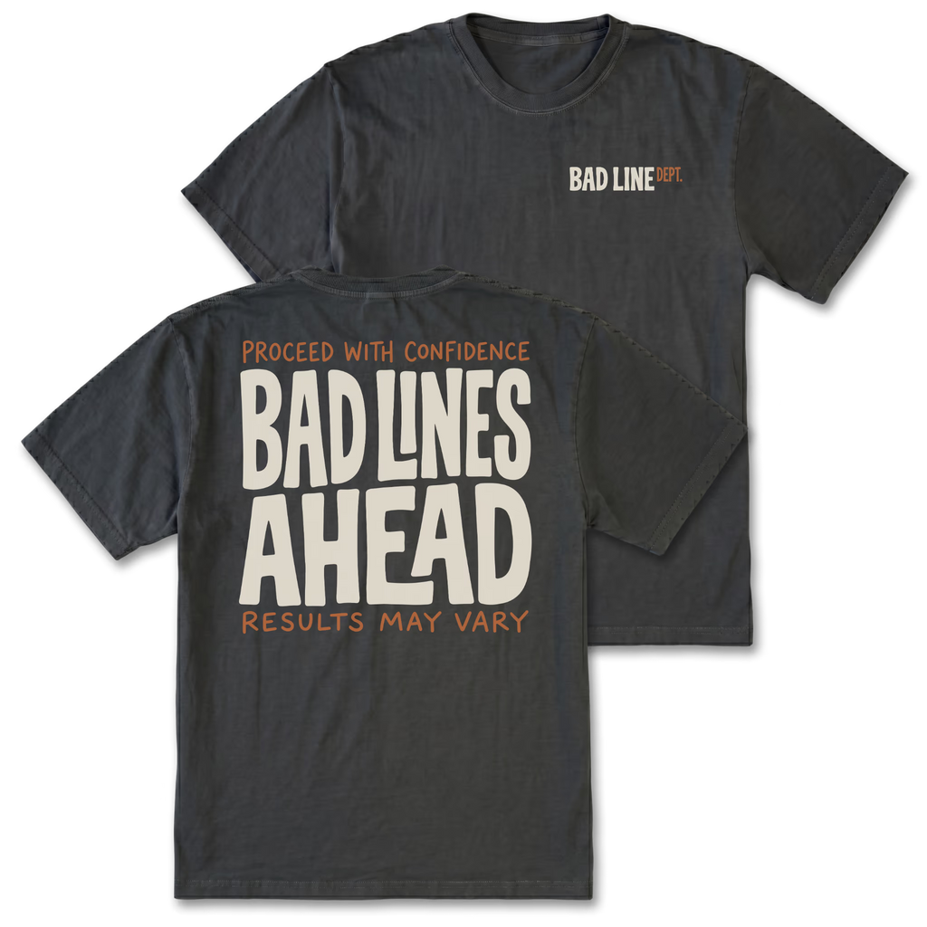 Two black graphic t-shirts shown on a white background, with the front and back views overlapping. The front features a small 'BAD LINE ART' logo on the left chest, and the back features a large graphic print reading 'PROCEED WITH CONFIDENCE BAD LINES AHEAD RESULTS MAY VARY' in cream and orange lettering.