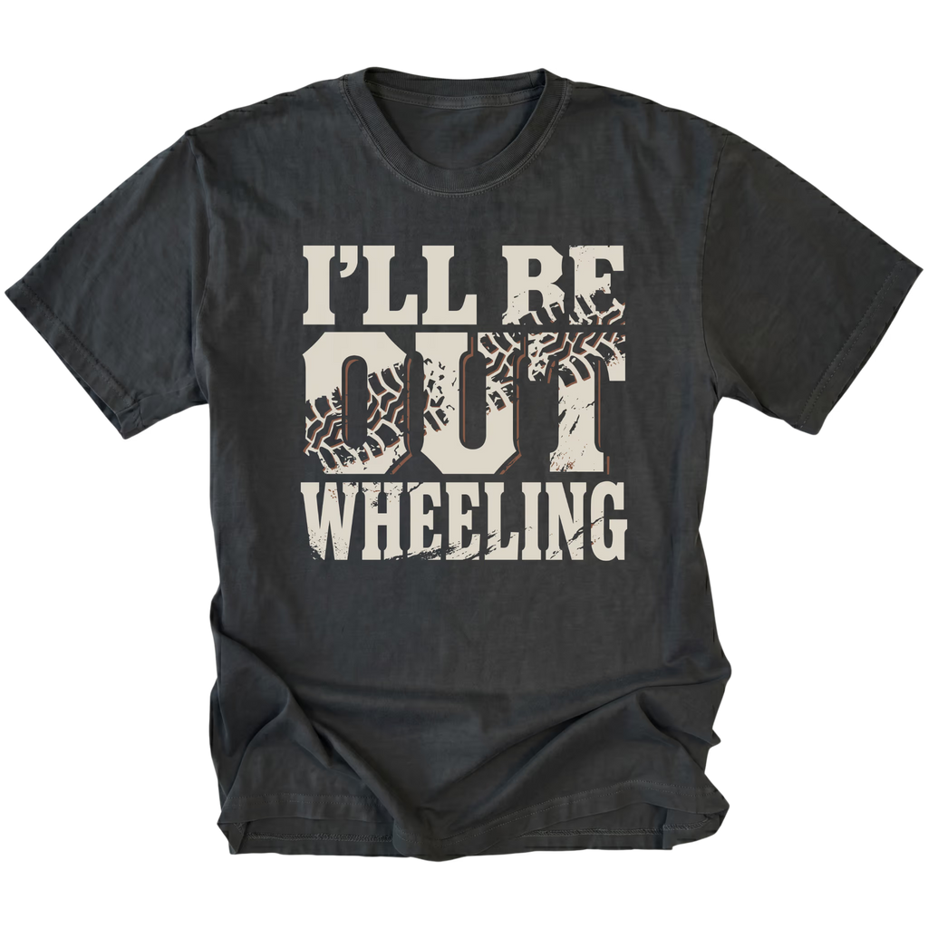 A black t-shirt with a distressed graphic on the front that reads 'I'LL BE OUT WHEELING' in cream-colored lettering, featuring tire tracks inside the letters 'O' and 'U'.