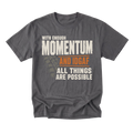 A charcoal gray crewneck t-shirt with a graphic print on the front. The text reads 'WITH ENOUGH MOMENTUM AND IDGAF ALL THINGS ARE POSSIBLE' in distressed white and orange lettering, with a faint tire track graphic behind it.