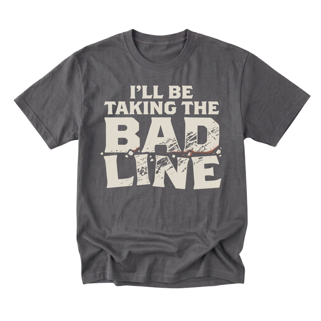 A charcoal gray crewneck t-shirt with a distressed cream-colored graphic text that reads 'I'LL BE TAKING THE BAD LINE' across the chest, displayed on a clean white background.