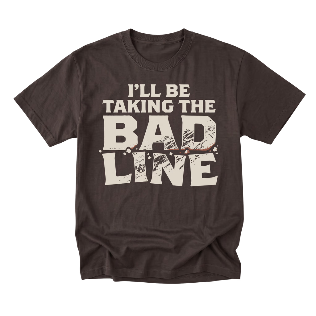 A dark brown short-sleeve t-shirt with a distressed graphic on the front that reads 'I'LL BE TAKING THE BAD LINE' in cream-colored text, displayed on a solid white background.