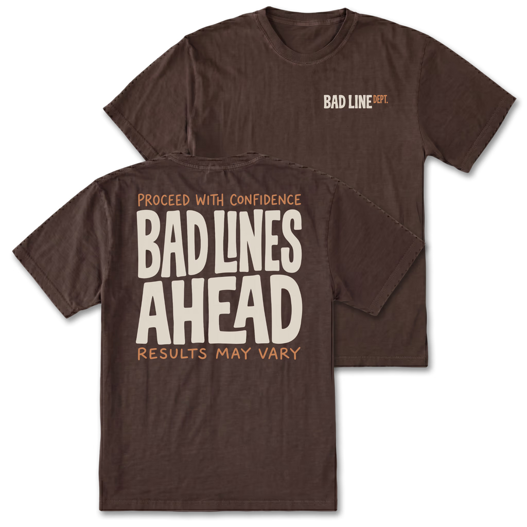 Two dark brown t-shirts shown on a white background, with the front and back views overlapping. The front features a small 'BAD LINE ART' logo on the left chest, and the back features a large graphic print reading 'PROCEED WITH CONFIDENCE BAD LINES AHEAD RESULTS MAY VARY' in cream and orange lettering.
