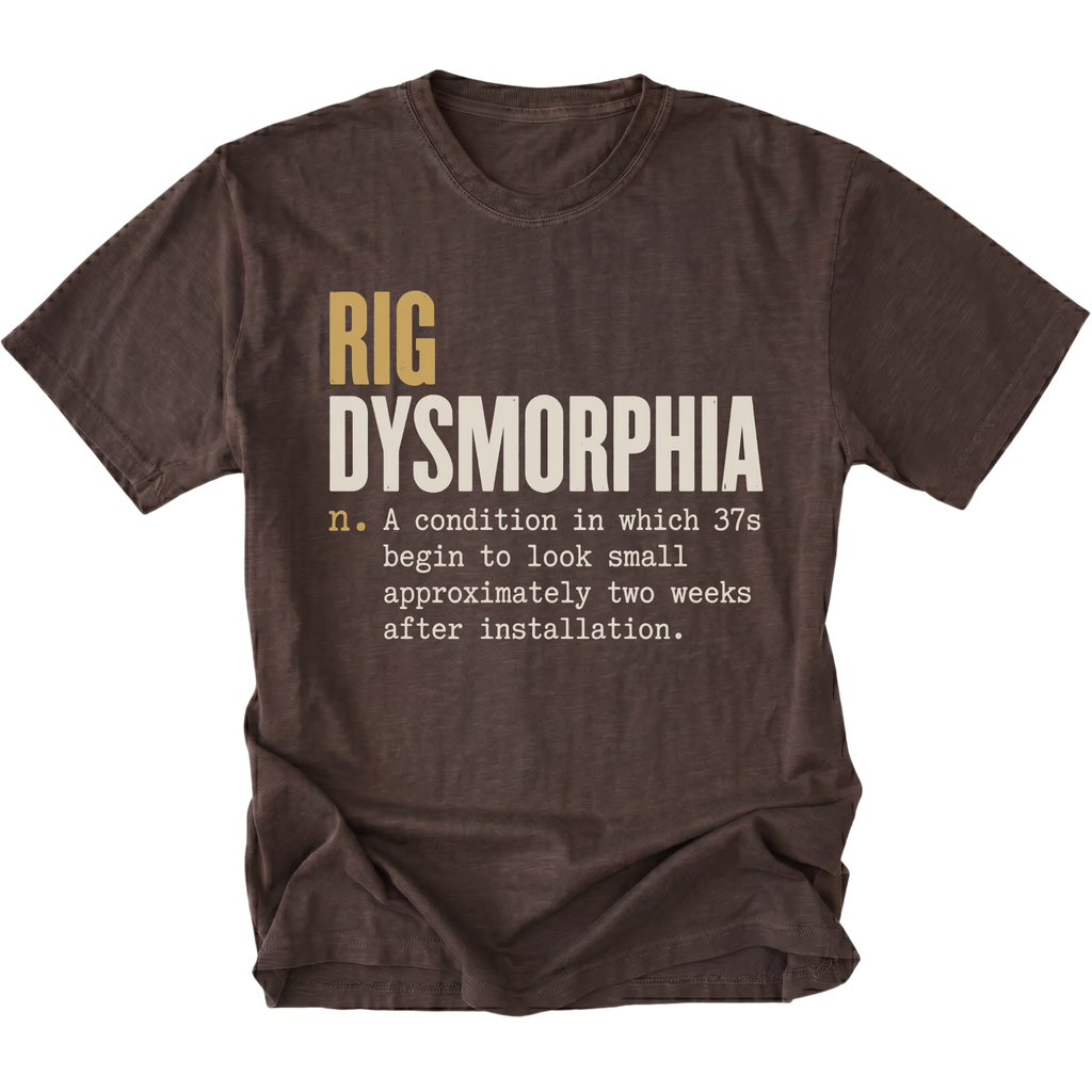A dark brown short-sleeve t-shirt with a humorous graphic print on the front. The text reads 'RIG DYSMORPHIA' in gold and white, followed by a definition in white typewriter font.