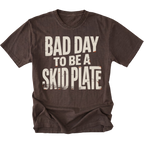 A dark brown short-sleeve t-shirt with a distressed white graphic text reading 'BAD DAY TO BE A SKID PLATE' on the front, displayed against a solid white background.