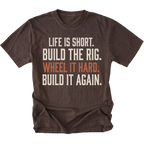 A dark brown short-sleeve t-shirt with a distressed white and orange text graphic on the front reading 'LIFE IS SHORT. BUILD THE RIG. WHEEL IT HARD. BUILD IT AGAIN.'