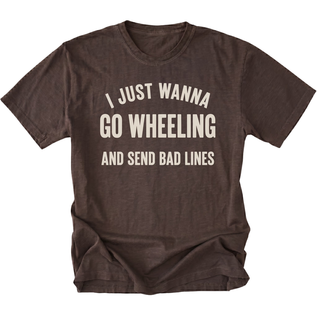 A dark brown t-shirt with distressed cream-colored text that reads 'I JUST WANNA GO WHEELING AND SEND BAD LINES' on a solid white background.