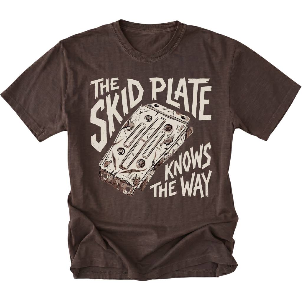 A dark brown short-sleeve t-shirt with a graphic print of a car wheel well and the text 'THE SKID PLATE KNOWS THE WAY' in a distressed off-white font, displayed flat against a white background.