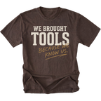 A dark brown heather t-shirt with a distressed graphic that reads 'WE BROUGHT TOOLS BECAUSE WE KNOW US.' in cream and tan lettering, displayed on a solid white background.