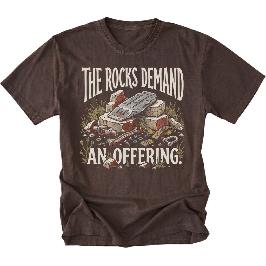 A dark brown short-sleeve t-shirt with a graphic print on the front. The graphic features the text 'THE ROCKS DEMAND AN OFFERING.