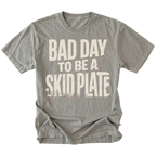 A gray short-sleeve t-shirt with a distressed white graphic text that reads 'BAD DAY TO BE A SKID PLATE' on the front, displayed against a solid white background.