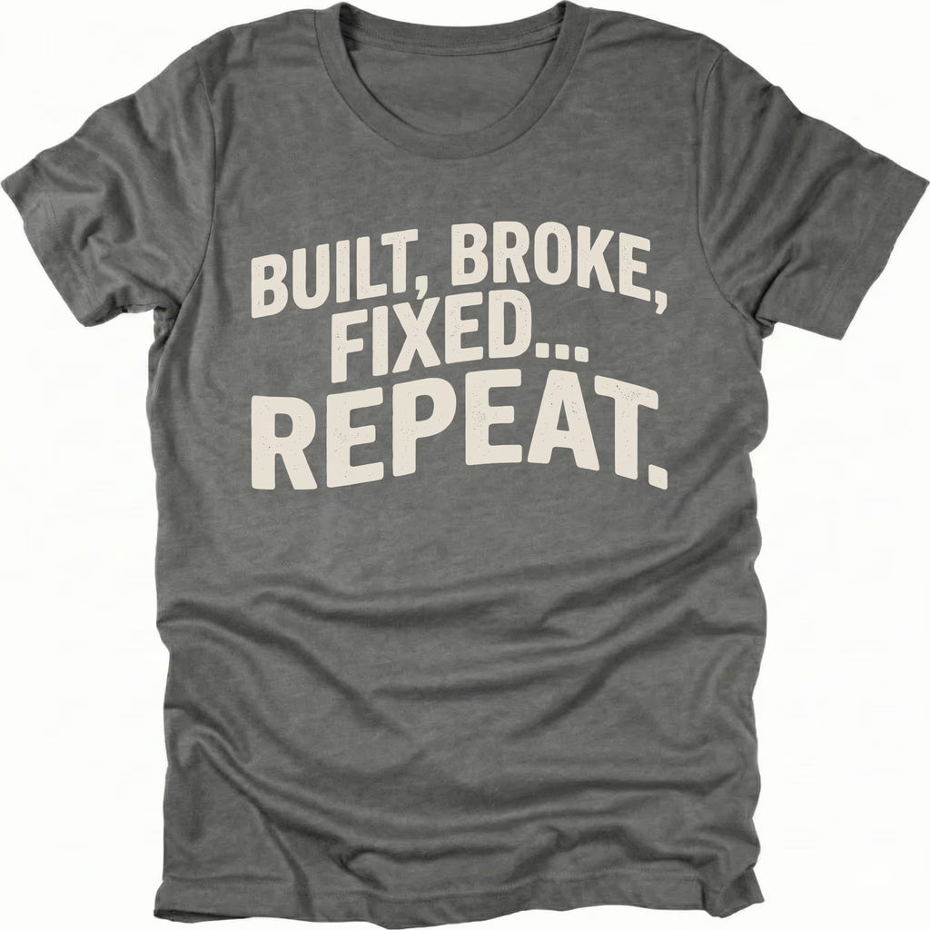 Grey t-shirt featuring built broke fixed repeat bold text graphic shown from the front by Trail Snark.