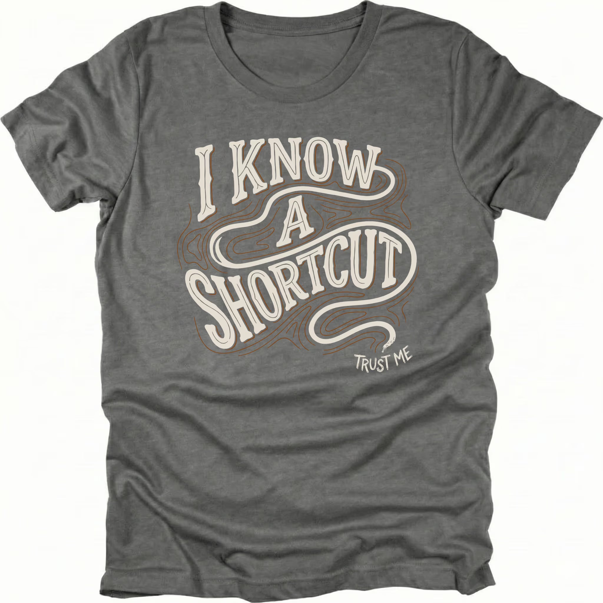 Grey t-shirt with vintage typography reading I Know A Shortcut Trust Me with winding trail lines, front view by Trail Snark.