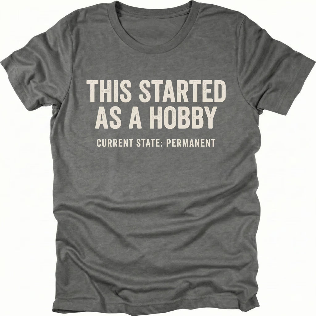 Grey t-shirt with text reading “This Started As a Hobby – Current State: Permanent” displayed on the front.