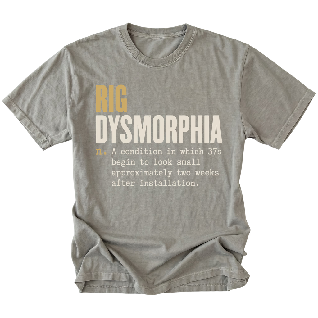 A gray short-sleeve t-shirt with a humorous graphic print on the front. The text reads 'RIG DYSMORPHIA' in gold and white, followed by a definition in white typewriter font.
