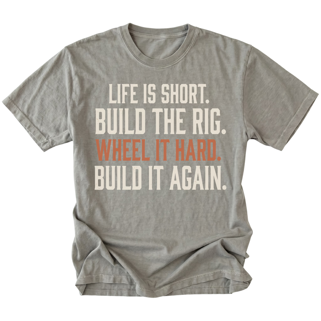 A gray short-sleeve t-shirt with a distressed white and orange text graphic on the front reading 'LIFE IS SHORT. BUILD THE RIG. WHEEL IT HARD. BUILD IT AGAIN.'