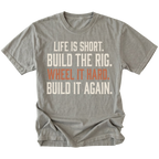 A gray short-sleeve t-shirt with a distressed white and orange text graphic on the front reading 'LIFE IS SHORT. BUILD THE RIG. WHEEL IT HARD. BUILD IT AGAIN.'