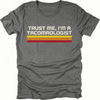 Grey t-shirt with retro stripes and the phrase “Trust Me, I’m a Tacomaologist” printed on the front by Trail Snark.