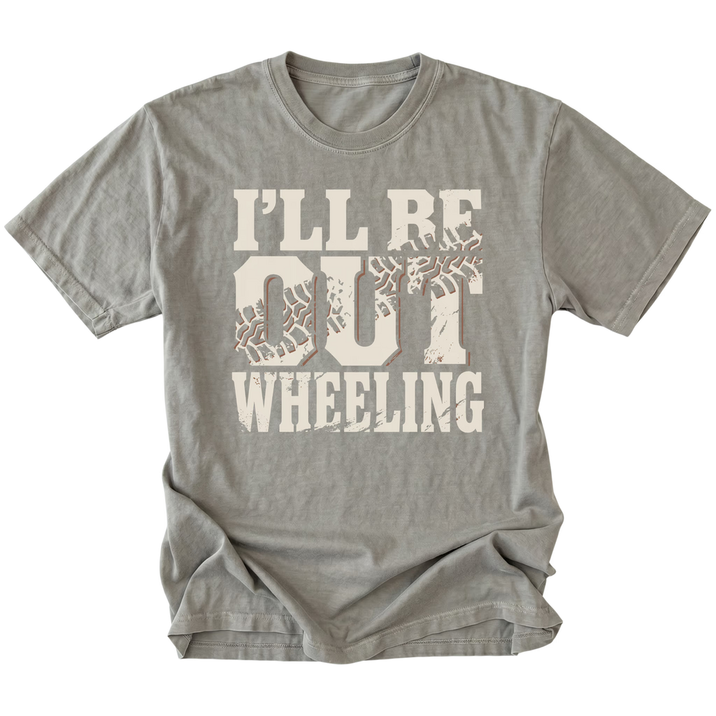 A gray crewneck t-shirt with a distressed graphic on the front that reads 'I'LL BE OUT WHEELING' in cream lettering, featuring tire tracks inside the letters 'OUT'.