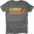 Grey t-shirt featuring all grown up still playing in the dirt retro stripe graphic shown from the front by Trail Snark.