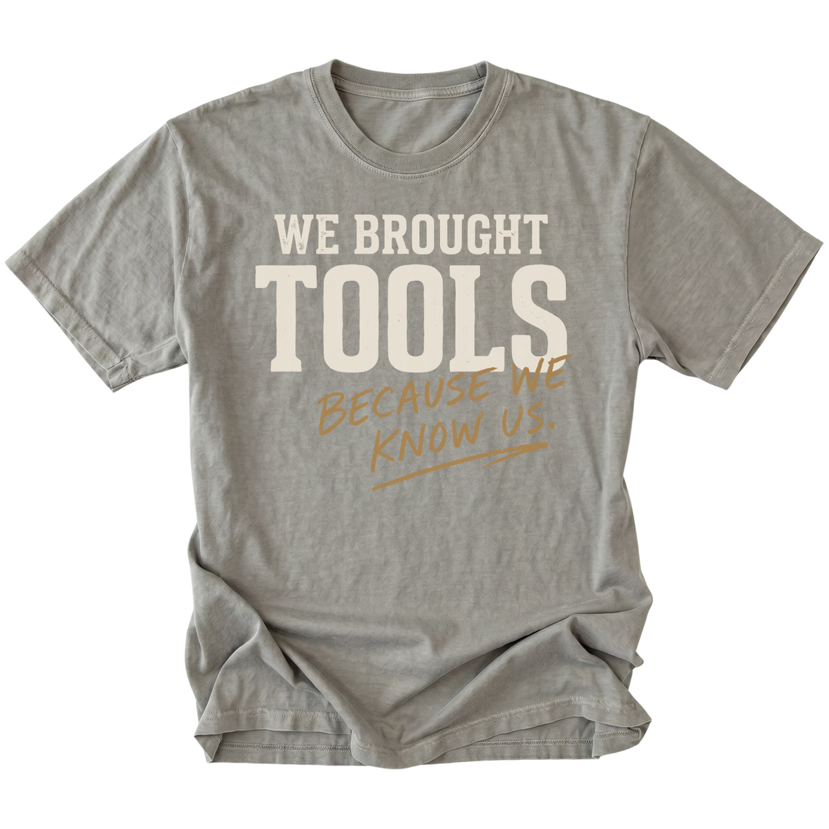 A gray short-sleeve t-shirt with a graphic text print reading 'WE BROUGHT TOOLS BECAUSE WE KNOW US.' in cream and tan lettering, displayed flat against a solid white background.