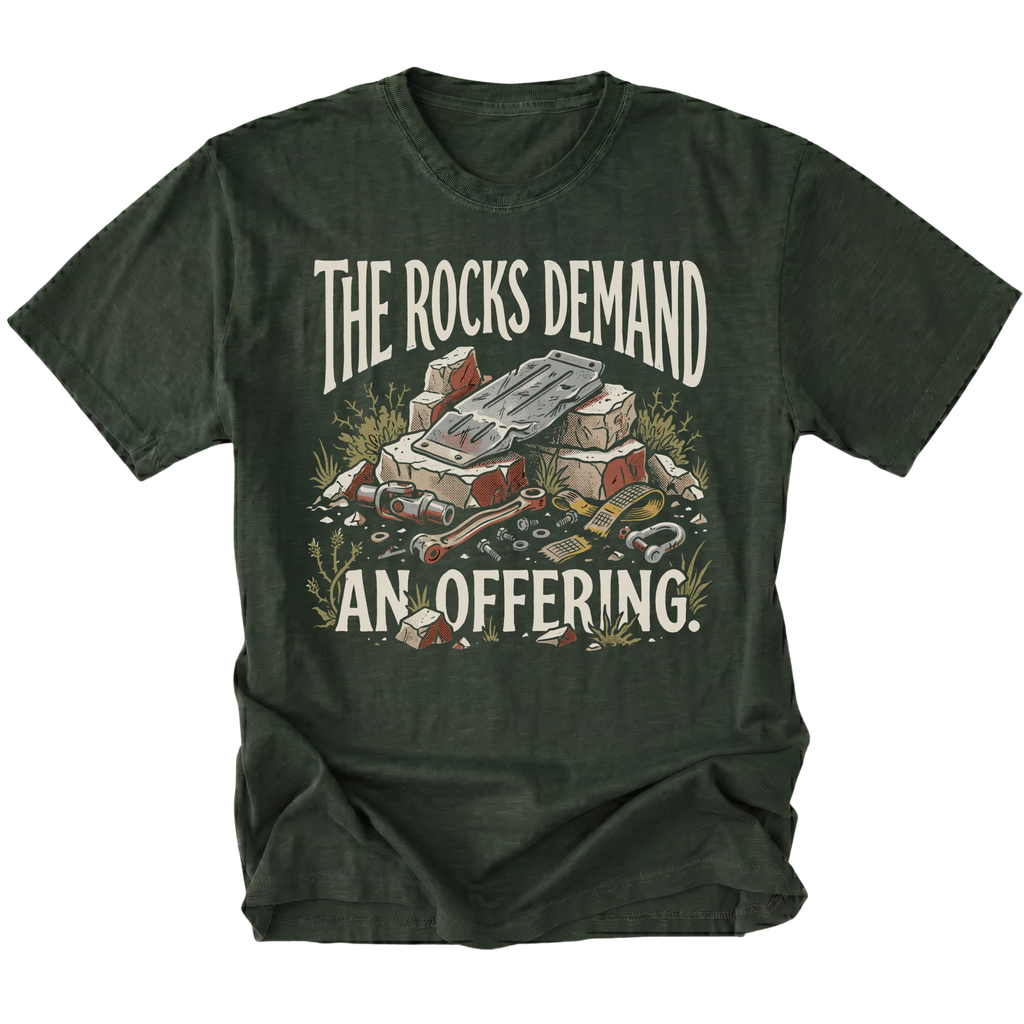 A moss green graphic t-shirt featuring a vintage-style illustration of a pile of rocks and mining tools, with the text 'THE ROCKS DEMAND AN OFFERING.' printed in distressed cream lettering.