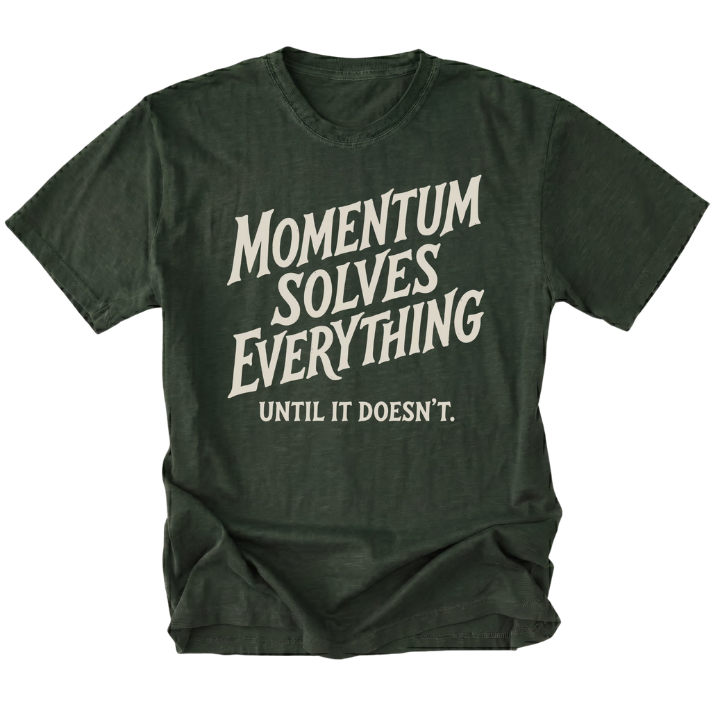 A moss green t-shirt with a distressed cream-colored graphic text that reads 'MOMENTUM SOLVES EVERYTHING UNTIL IT DOESN'T.' on a solid white background.