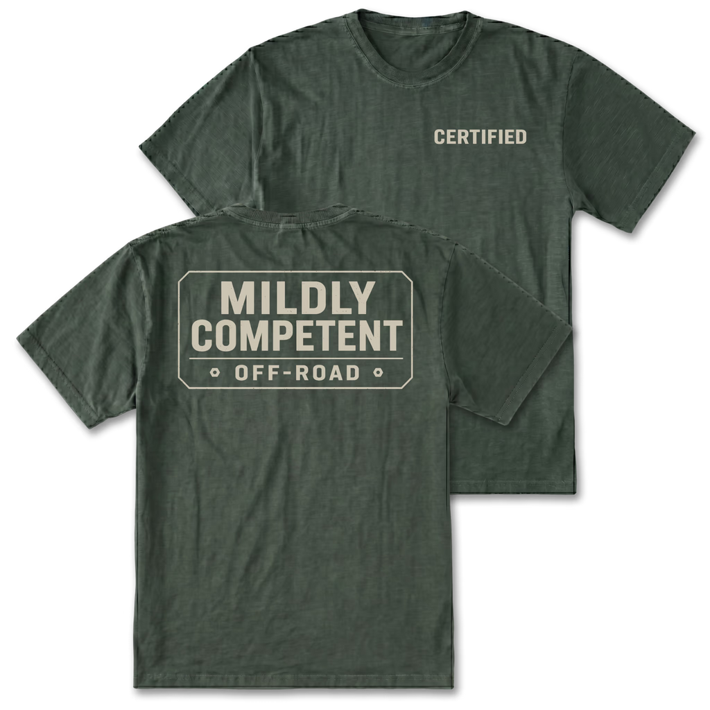Two views of a moss green t-shirt on a white background. The front view shows the word 'CERTIFIED' printed in beige on the left chest, while the back view shows a large beige graphic in the shape of a road sign that reads 'MILDLY COMPETENT OFF-ROAD'.