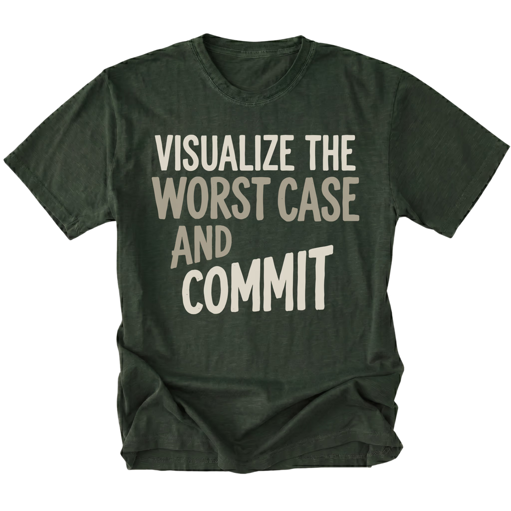 A moss green short-sleeve t-shirt with the phrase 'VISUALIZE THE WORST CASE AND COMMIT' printed in a light beige, hand-drawn style font across the chest, displayed on a clean white background.