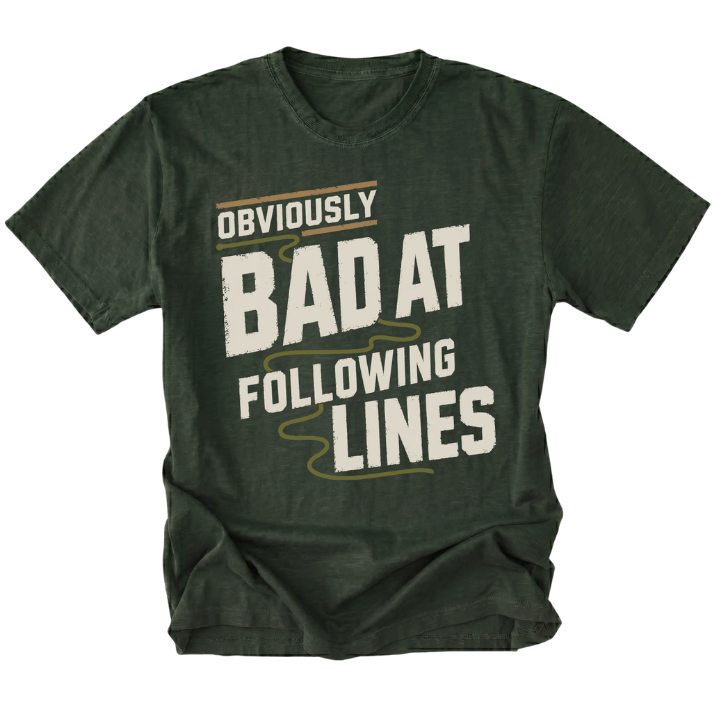 A moss green t-shirt with a distressed graphic print that reads 'OBVIOUSLY BAD AT FOLLOWING LINES' in cream and light olive lettering, displayed on a solid white background.