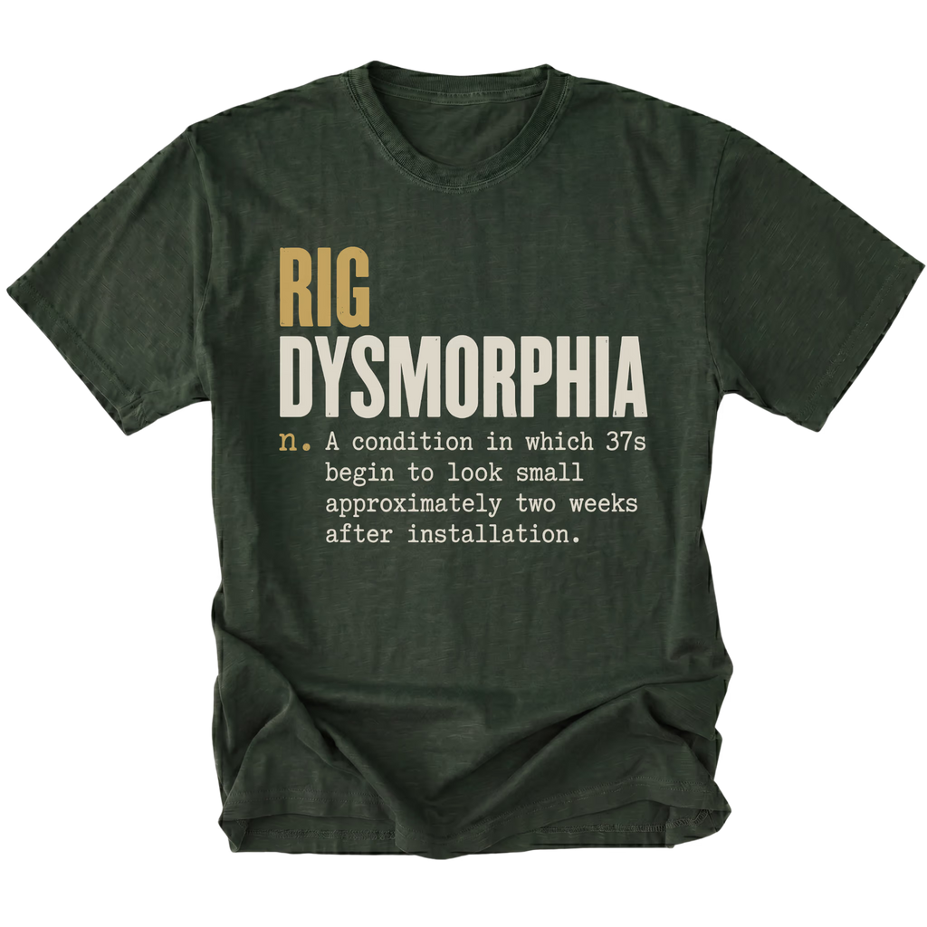 A moss green short-sleeve t-shirt with a humorous graphic print on the front. The text reads 'RIG DYSMORPHIA' in gold and white, followed by a definition in white typewriter font.
