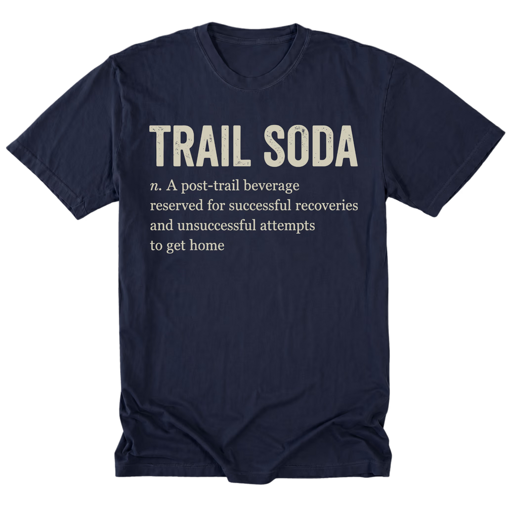 A navy blue short-sleeve t-shirt with a humorous dictionary-style definition printed on the front. The text reads 'TRAIL SODA' in large cream-colored letters, followed by 'n.