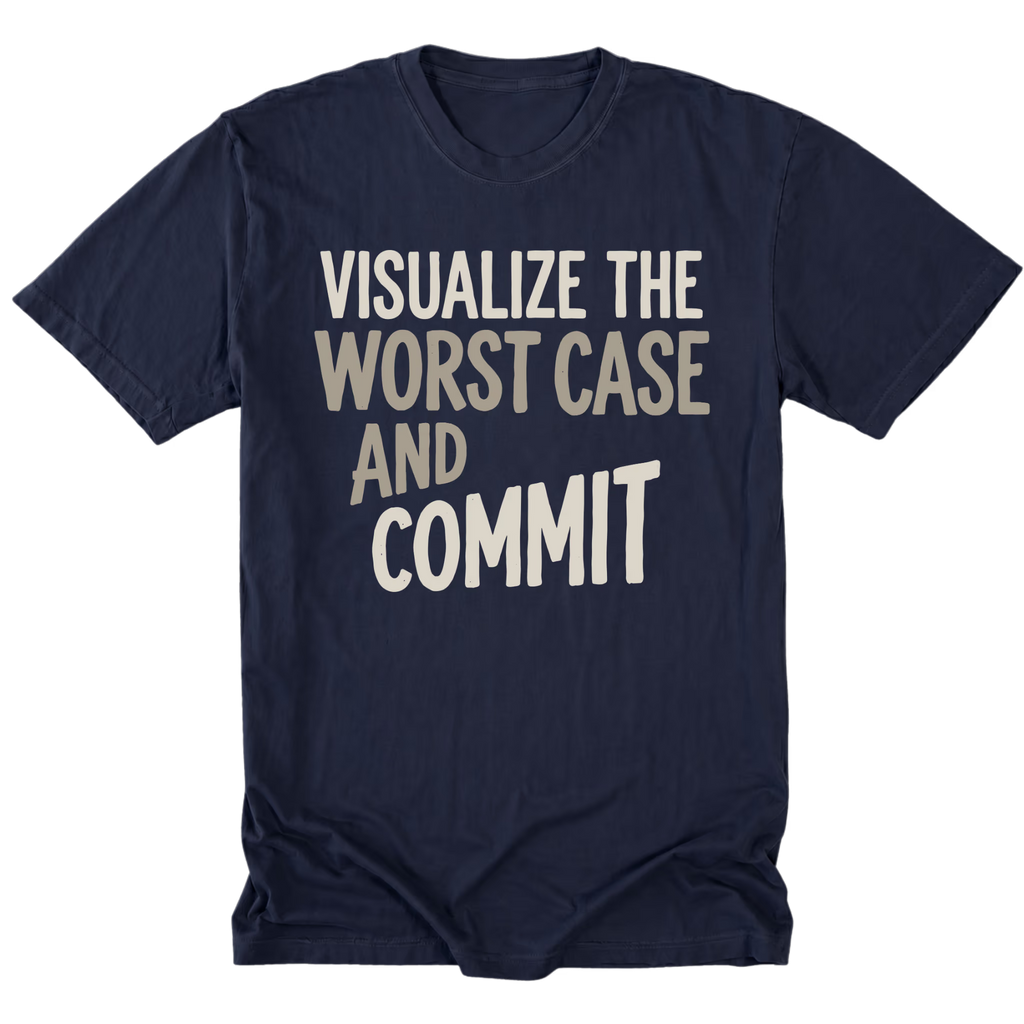 A navy blue tall short-sleeve t-shirt with the phrase 'VISUALIZE THE WORST CASE AND COMMIT' printed on the front in a light beige and white sans-serif font, shown against a plain white background.