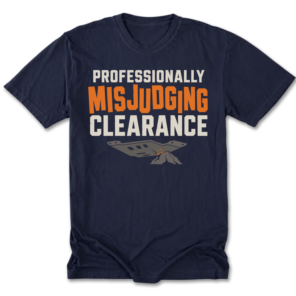 A navy blue short-sleeve t-shirt with a graphic print on the front reading 'PROFESSIONALLY MISJUDGING CLEARANCE' in white and orange lettering, with a gray and orange parachute graphic below, shown on a plain white background.