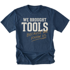 A navy blue short-sleeve t-shirt with a graphic text print reading 'WE BROUGHT TOOLS BECAUSE WE KNOW US.' in white and gold lettering, displayed on a clean white background.