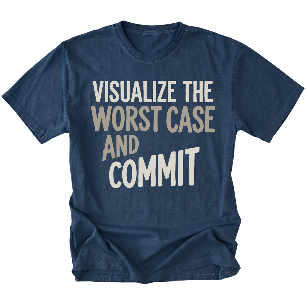 A navy blue short-sleeve t-shirt with a graphic text print reading 'VISUALIZE THE WORST CASE AND COMMIT' in cream and light beige lettering, displayed on a clean white background.
